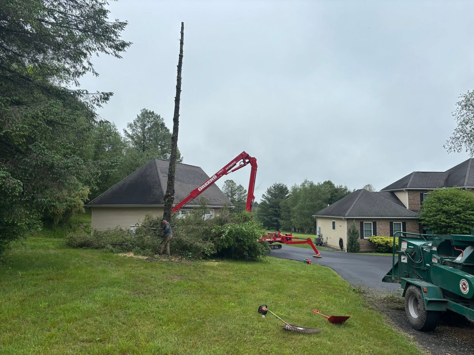 Tree being cut down by a crane next to a house on a cloudy day.
