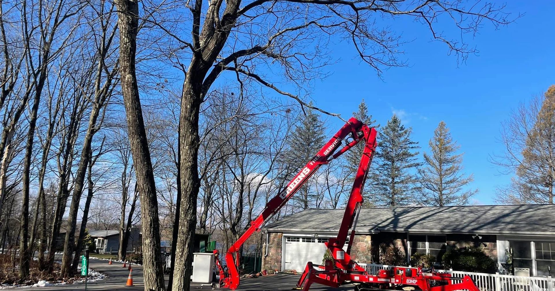 A red tree-trimming machine working on a tree near a house on a sunny day.