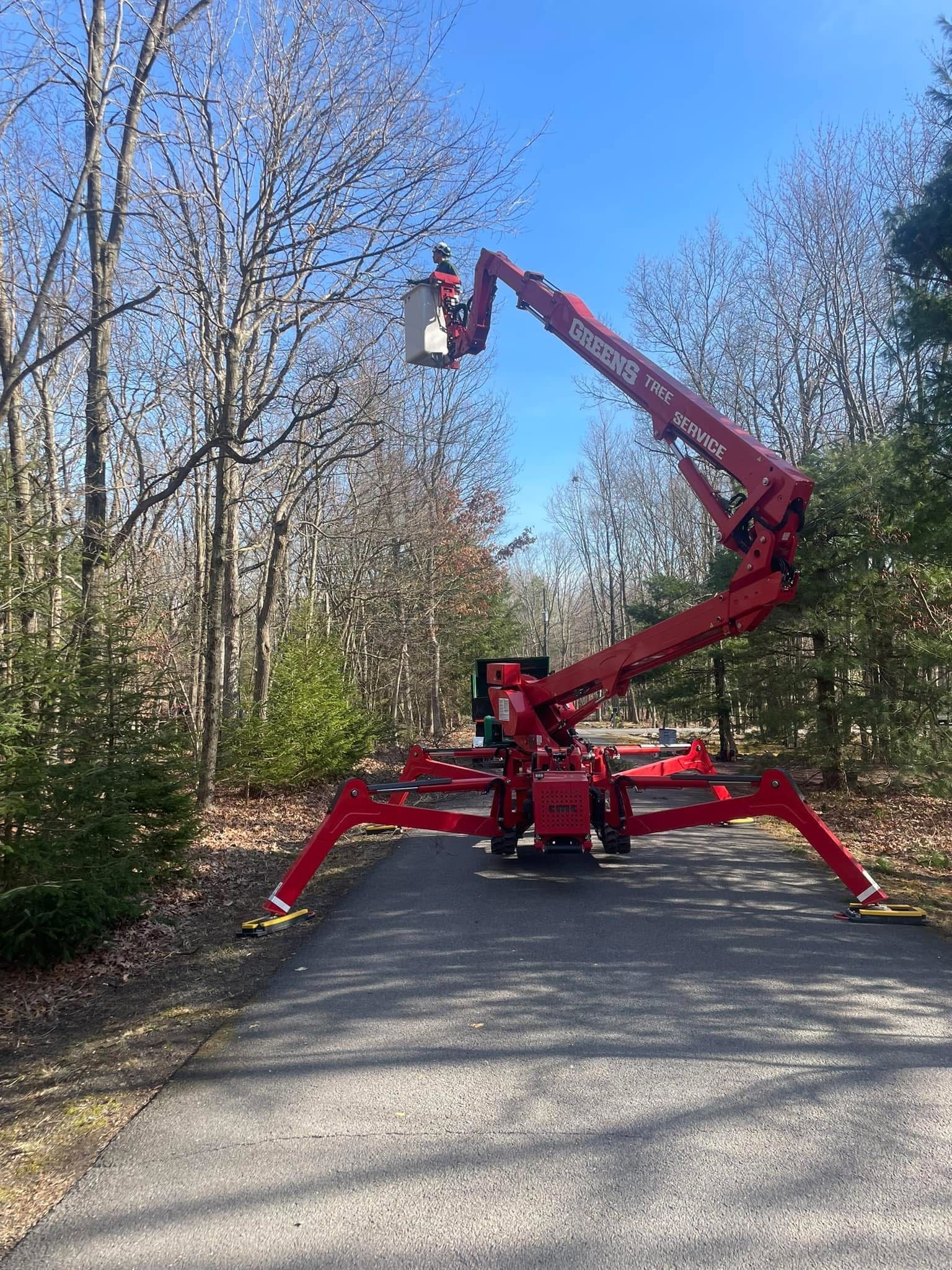 Red tree lift on a paved driveway in a wooded area under a blue sky.