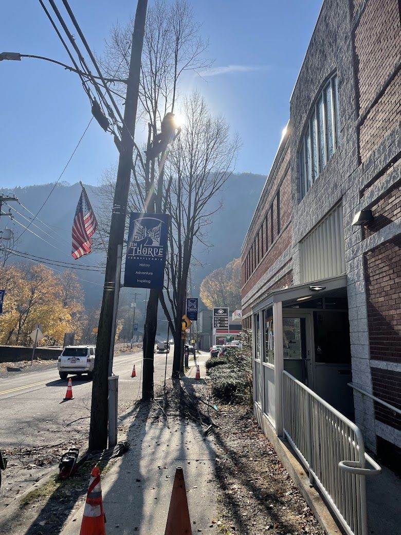 Sunny street scene with buildings, power lines, road, mountain backdrop, and banners.