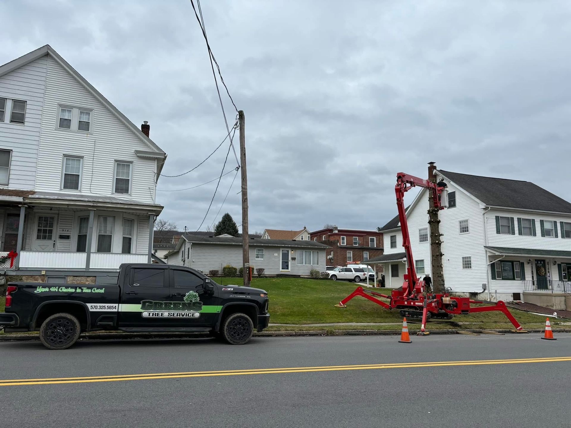 Utility truck and crane working on power lines next to houses under an overcast sky.