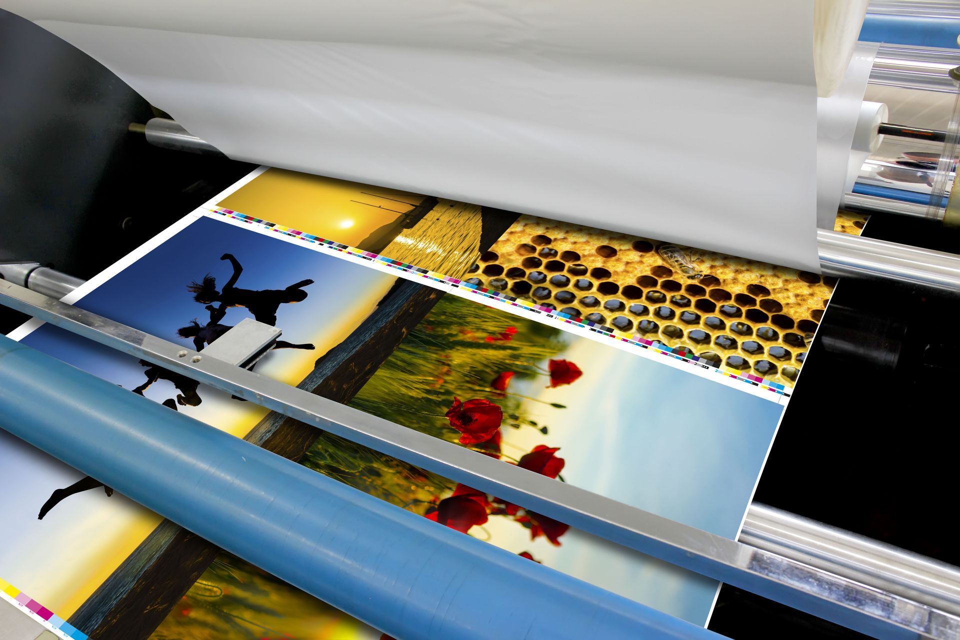 A printing press laminating colorful photos, including nature scenes, on a black surface.