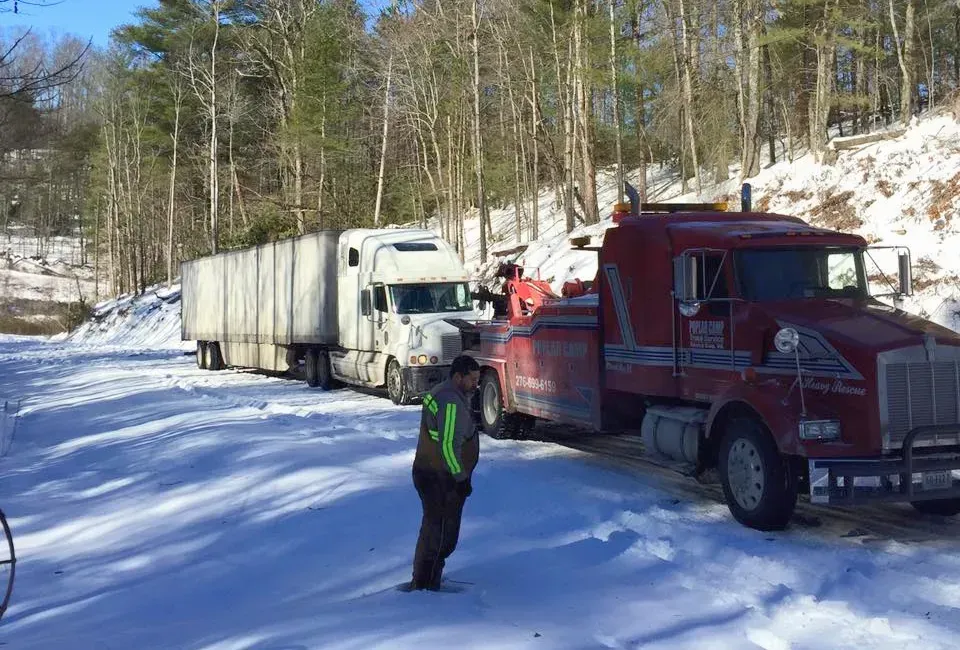 A man is standing next to a tow truck in the snow.