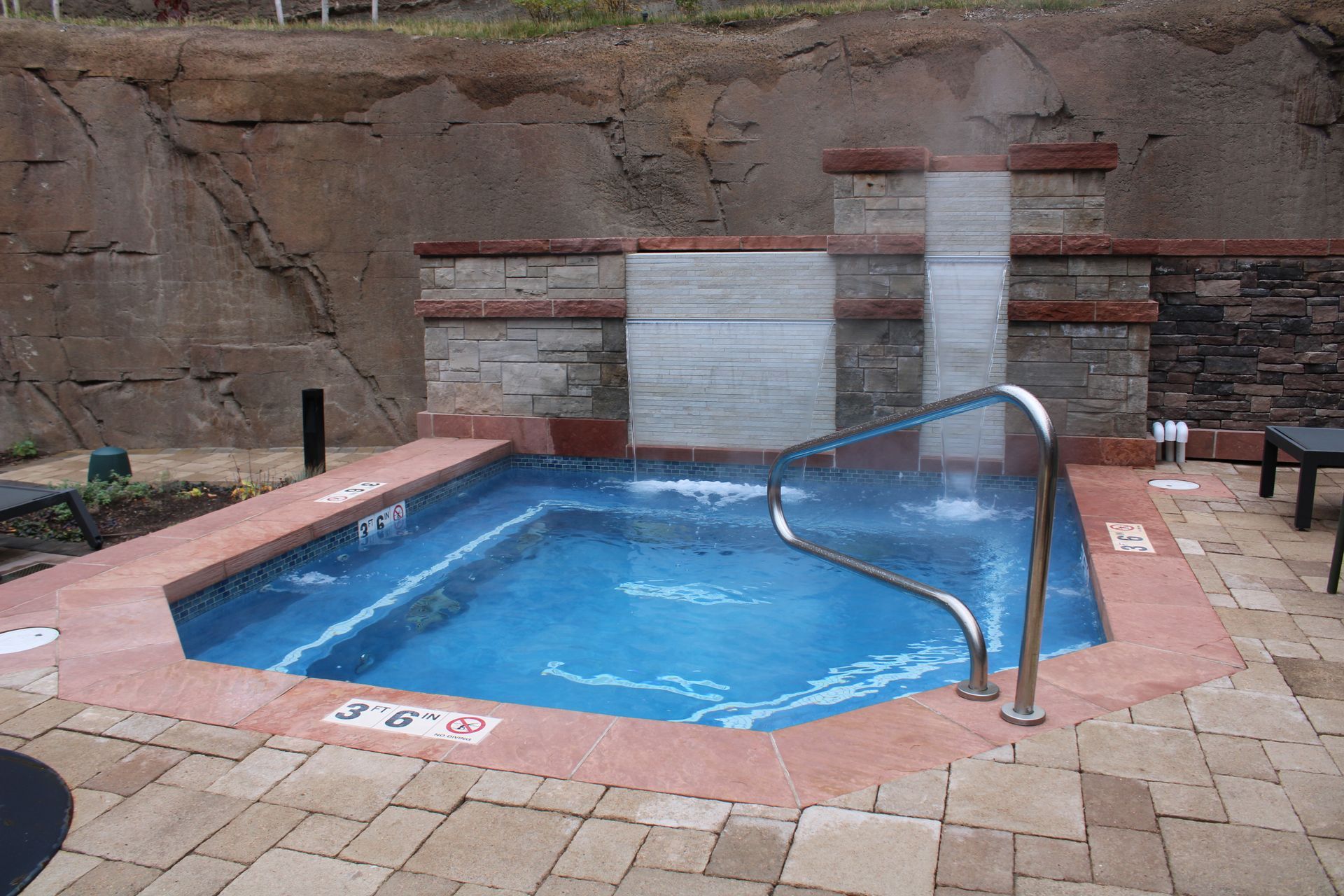 Small outdoor hot tub with blue water, waterfall feature, and stone surround.