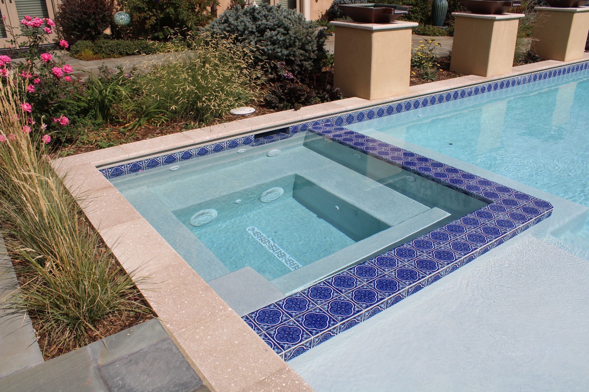 A swimming pool with an attached hot tub, blue tile border, and beige deck.