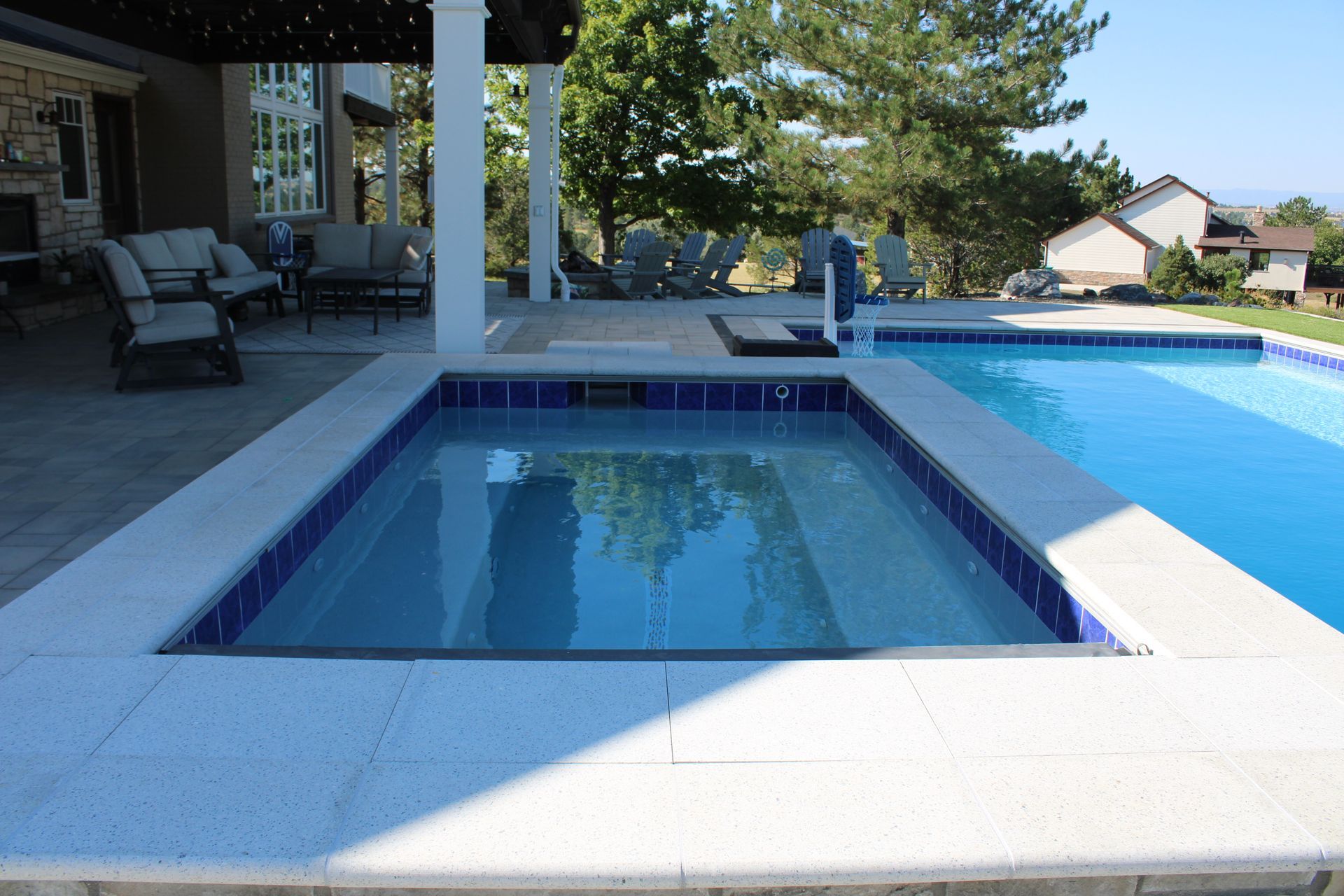 Hot tub next to a pool with a patio and house in the background on a sunny day.