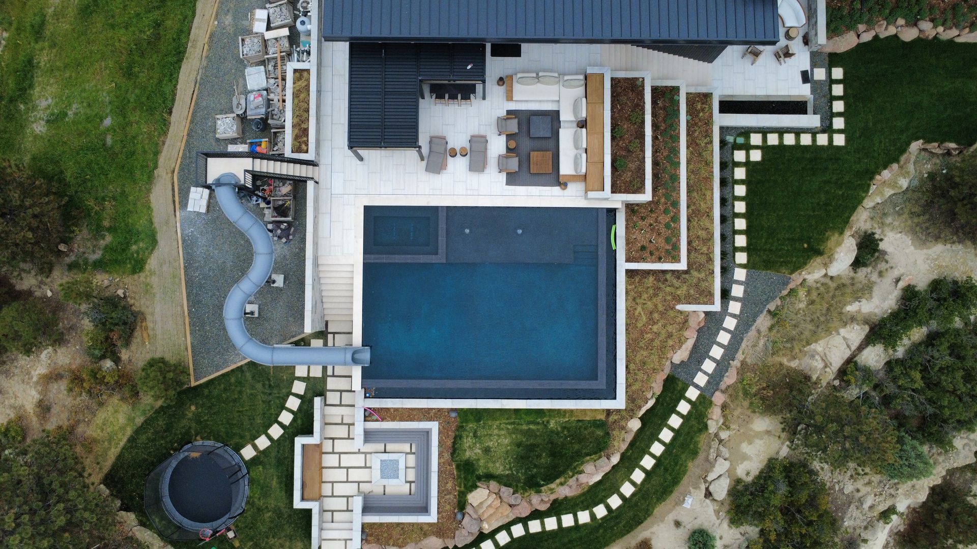 Aerial view of modern house with pool and outdoor seating area on a grassy hillside.