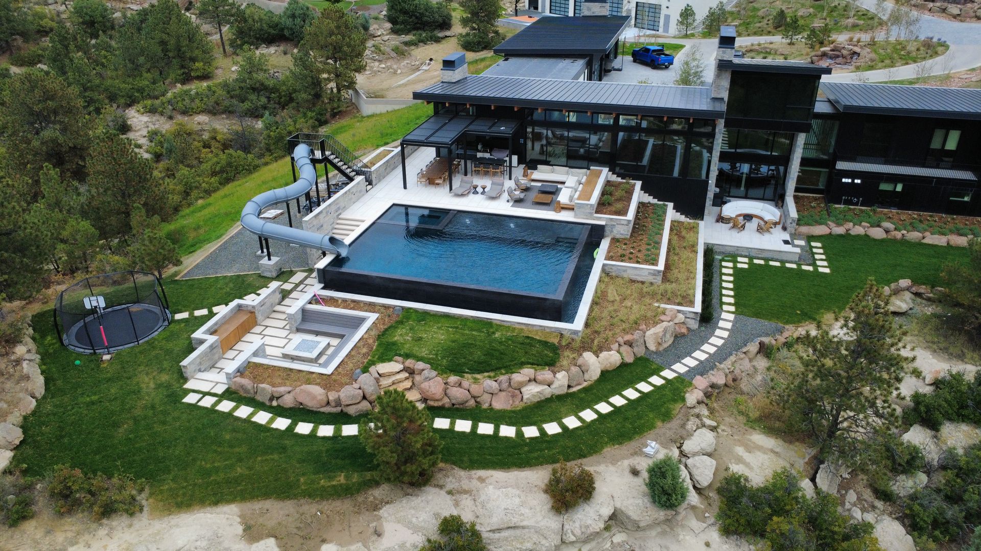 Modern home with dark exterior, pool, slide, fire pit, and stone pathway.