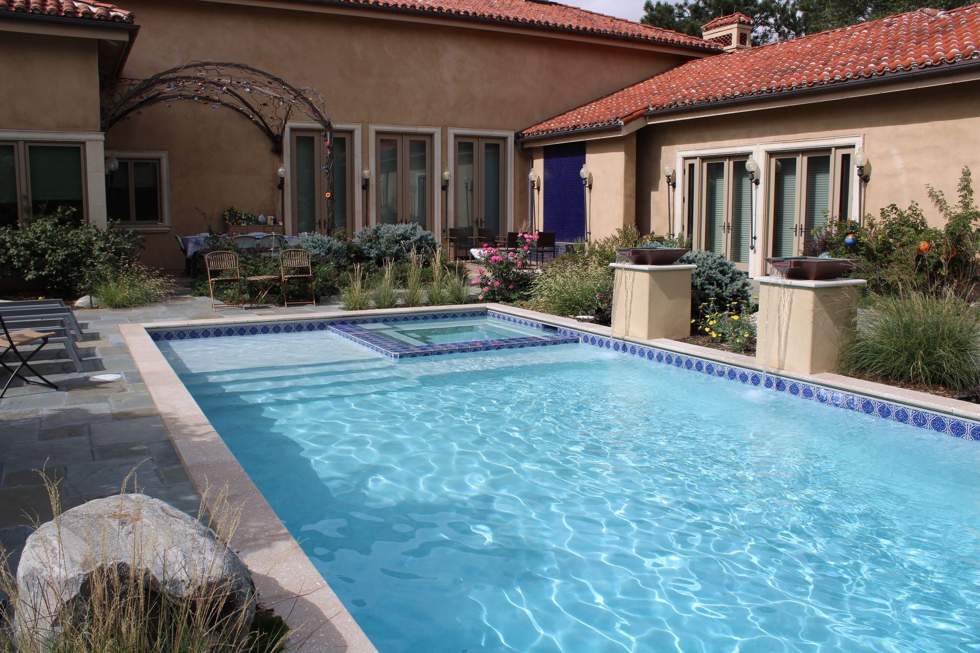 Backyard with a swimming pool, spa, and house with a terracotta tile roof.