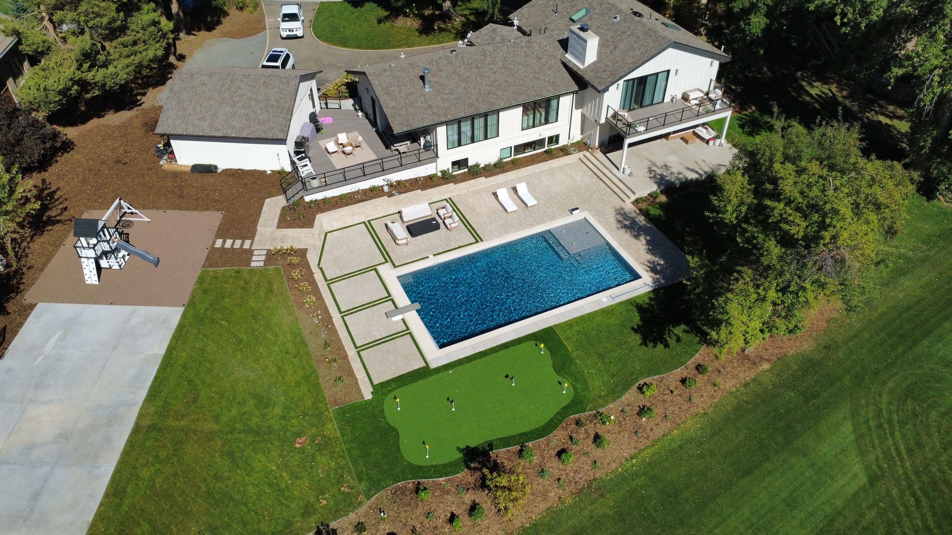 Aerial view of a modern white house with a pool, patio, and putting green on a grassy lawn.