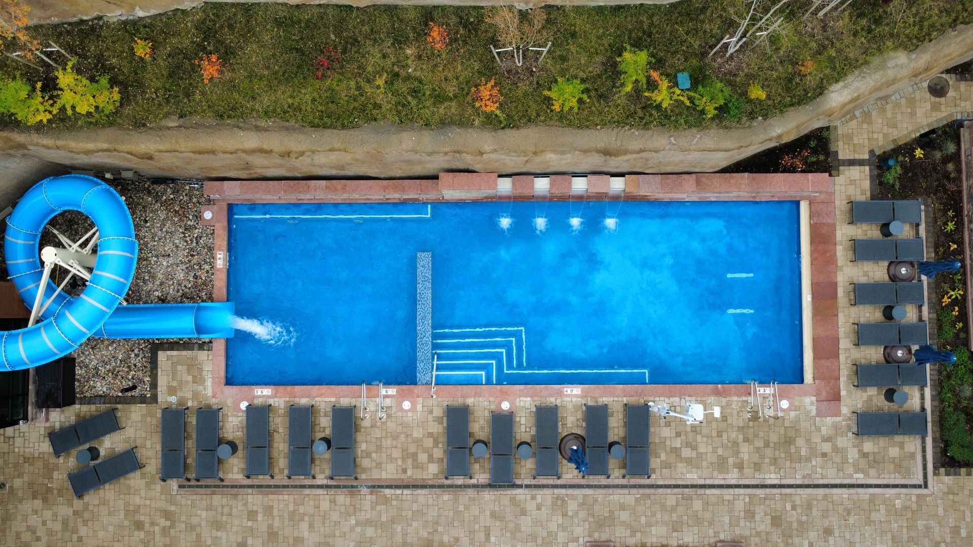 Aerial view of a rectangular pool with a blue slide, surrounded by lounge chairs and greenery.