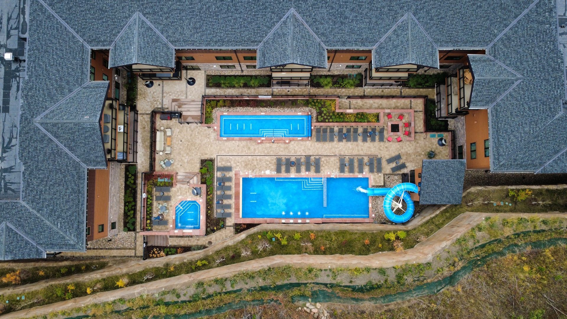 Aerial view of a complex with two pools, a water slide, and lounge chairs.