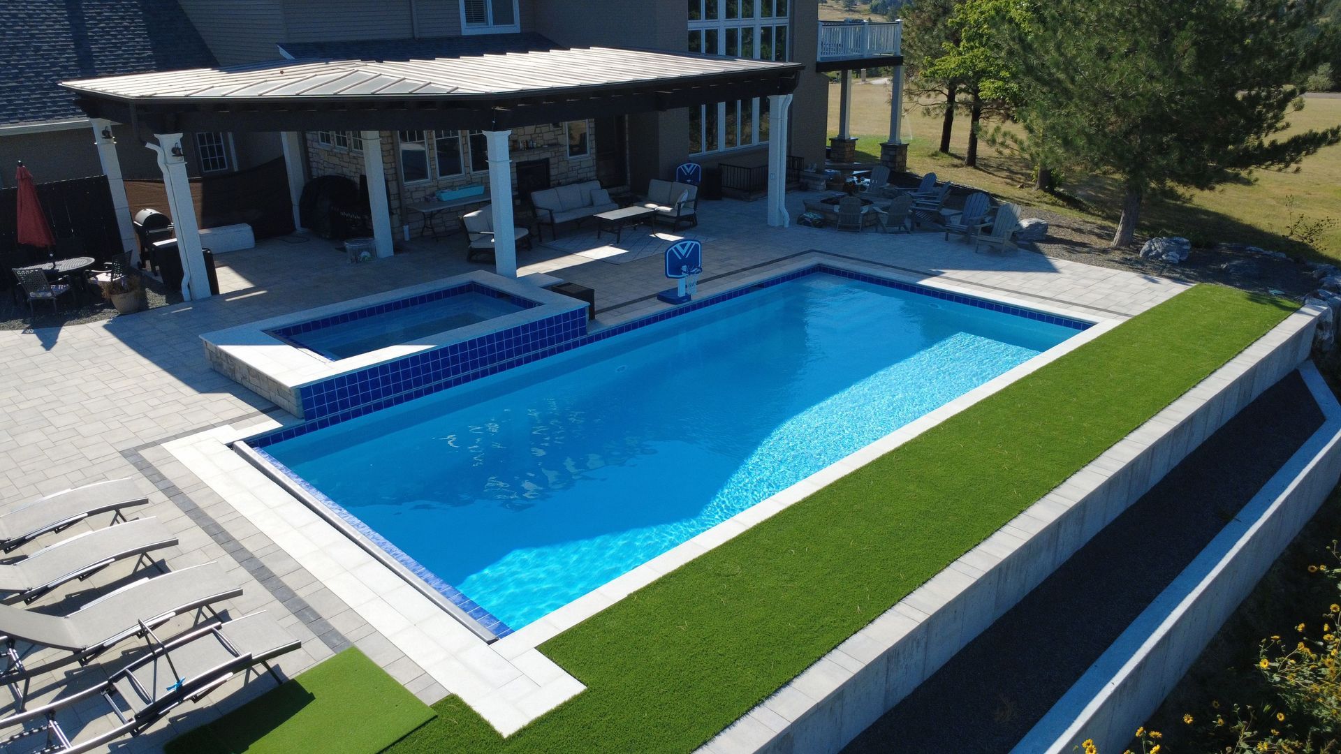 Backyard pool with spa, pergola, and artificial turf in a sunny setting.