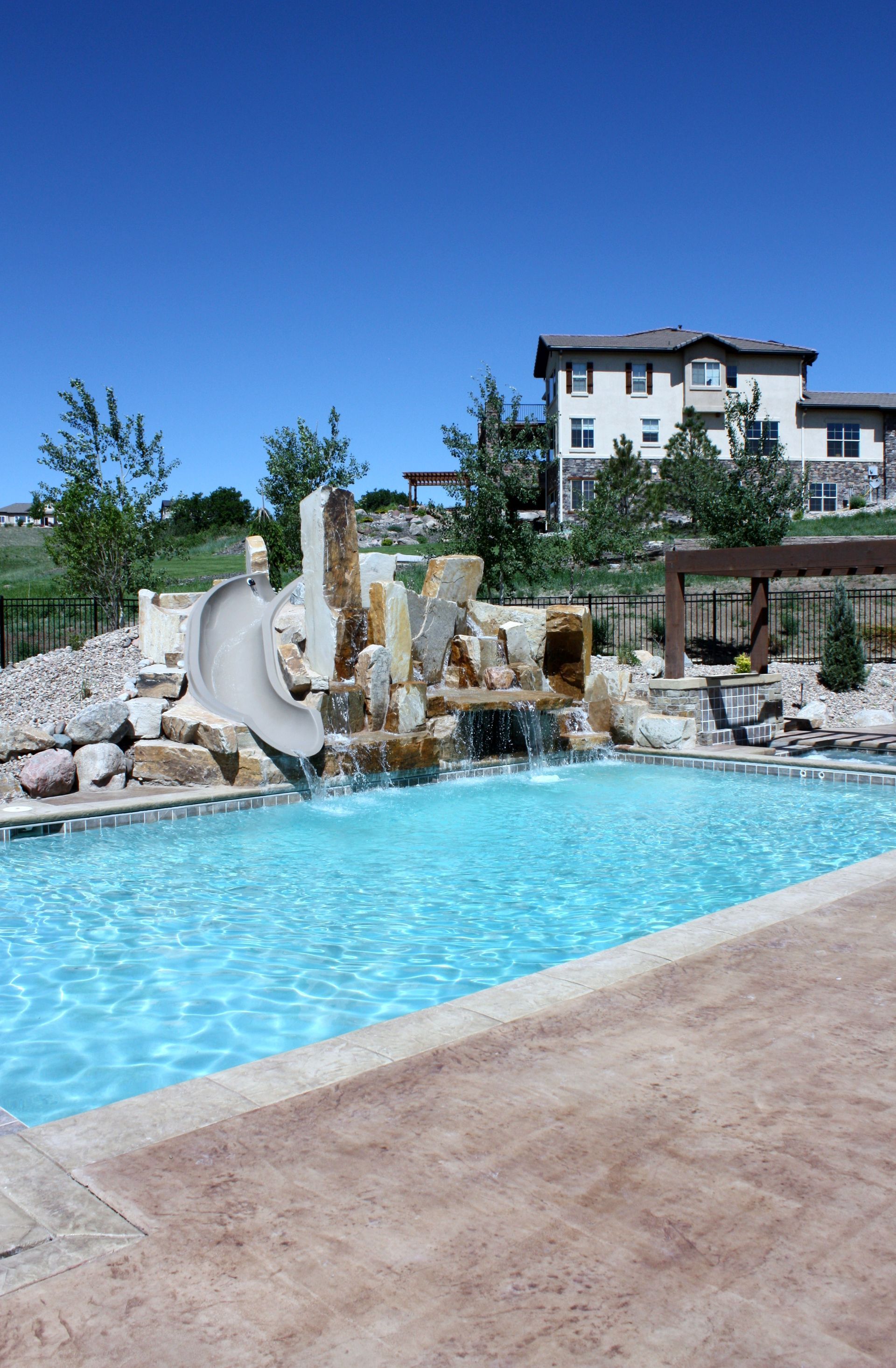 A large swimming pool with a water slide and a house in the background