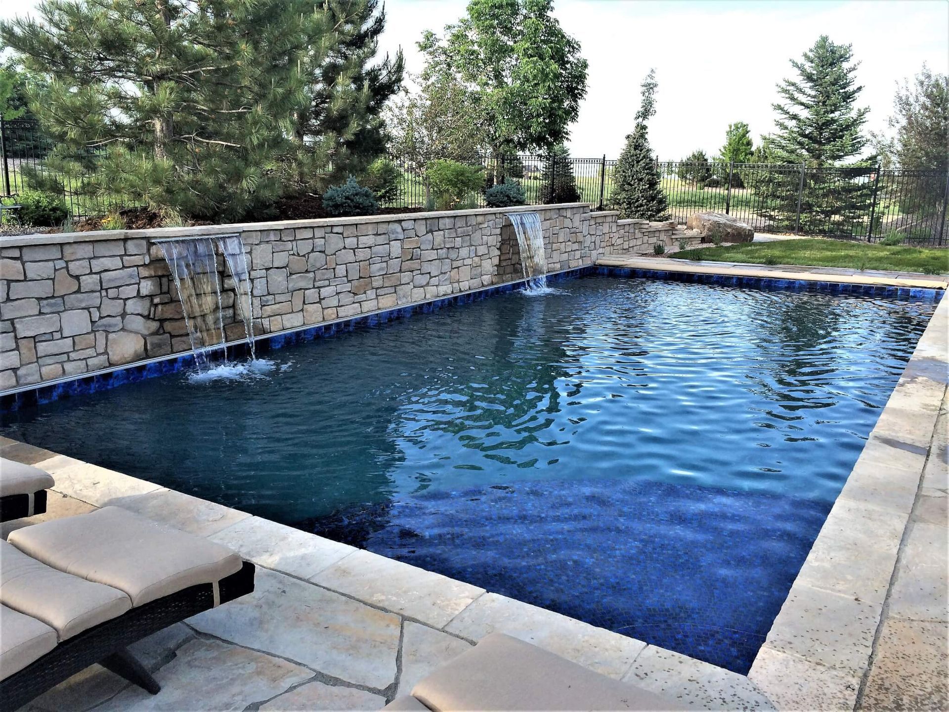 A large swimming pool with a waterfall and a stone wall surrounding it.