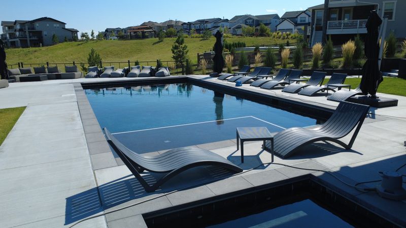 A rectangular outdoor pool with lounge chairs on a sunny day in a suburban setting.