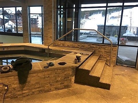 A hot tub with stairs and a railing in a room with a lot of windows.