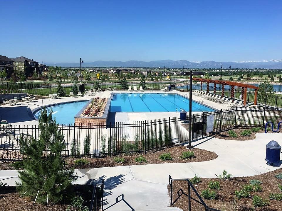 A large swimming pool surrounded by a fence in a park with mountains in the background.