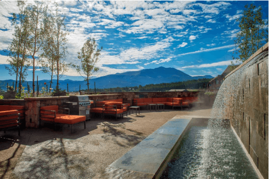 There is a waterfall in the middle of a patio with mountains in the background.