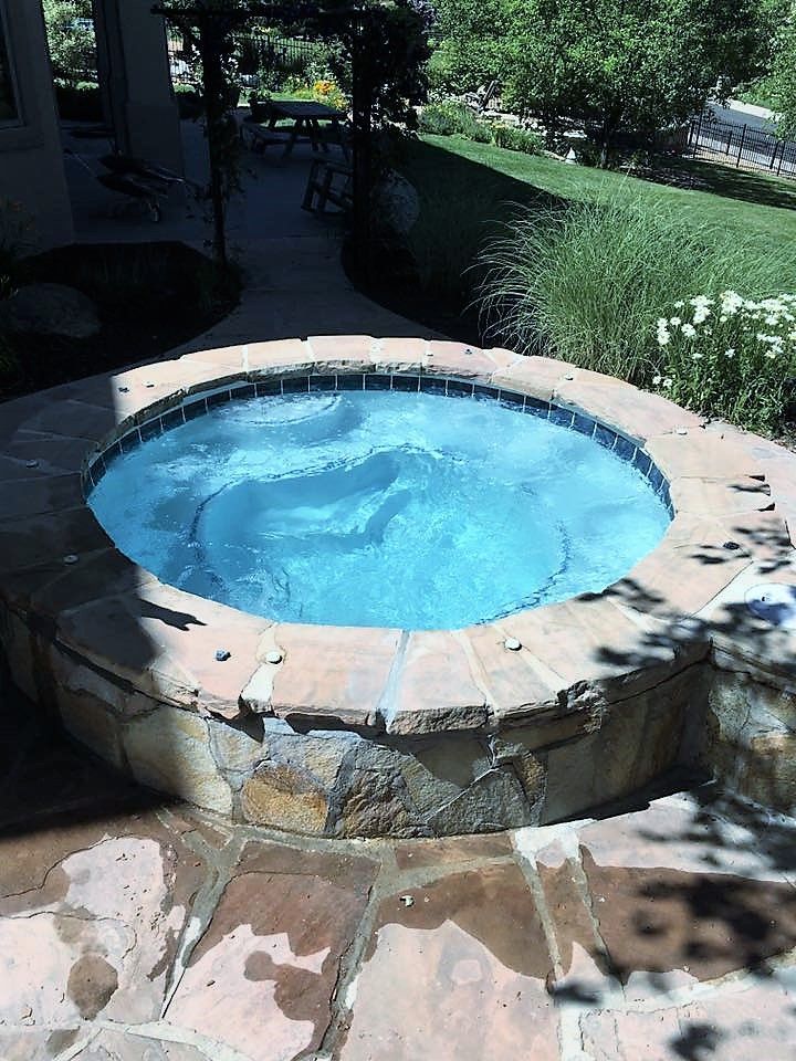 A round hot tub is surrounded by stone steps and trees.