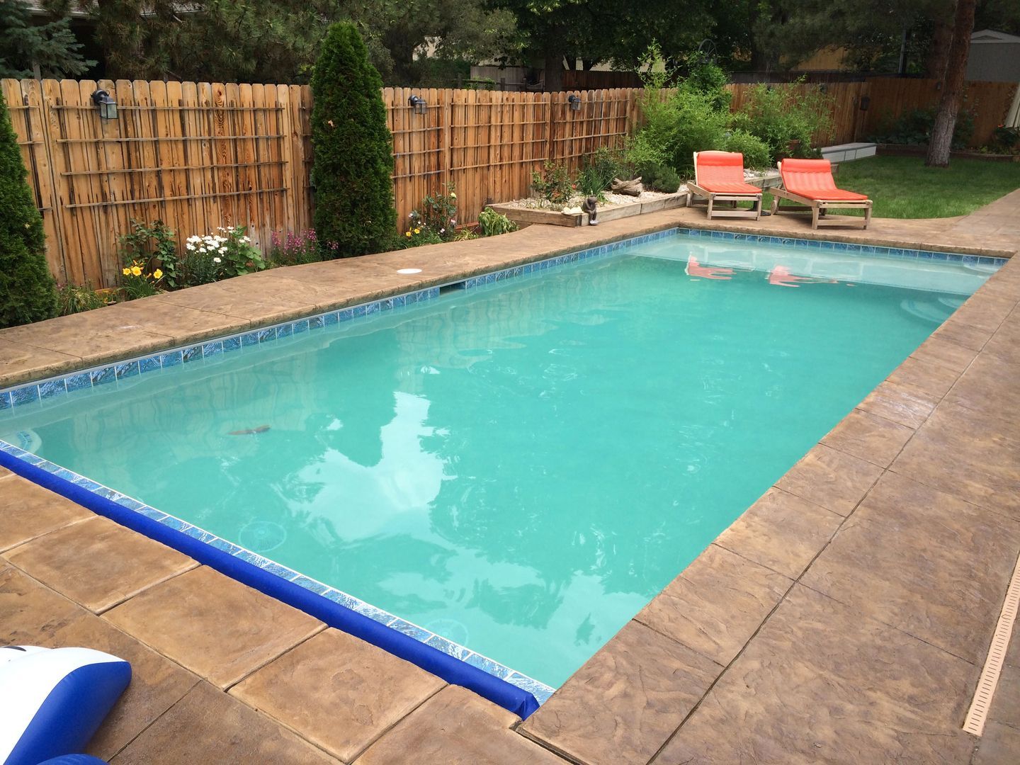 A large swimming pool is surrounded by chairs and a wooden fence.