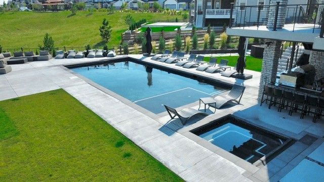 Outdoor pool with adjacent hot tub, surrounded by lounge chairs and greenery.