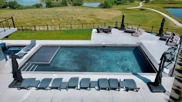 Poolside scene with a rectangular pool, lounge chairs, and outdoor seating area overlooking a grassy landscape.