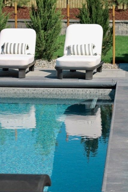 Two white lounge chairs with striped pillows near a pool, with reflections in the water.