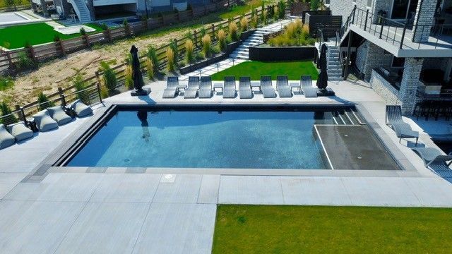 An aerial view of a luxury pool with lounge chairs, patio, and modern house.