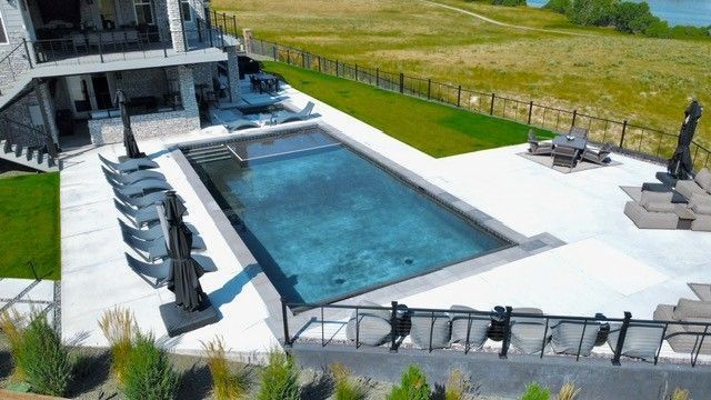 An outdoor pool next to a house, with lounge chairs and a grassy landscape in the background.