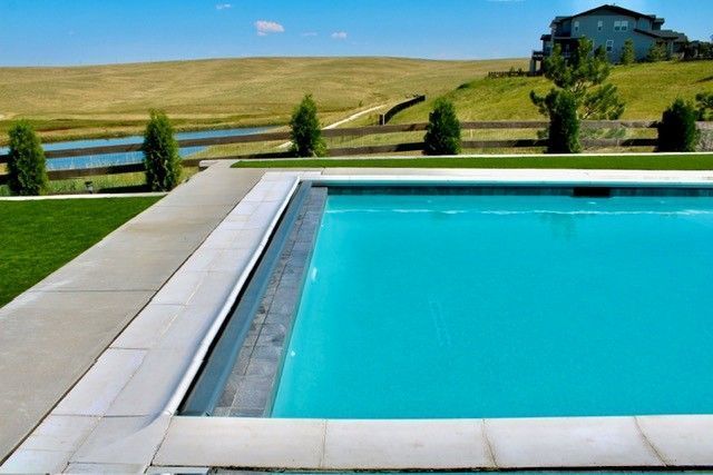 A turquoise swimming pool with a concrete border and a scenic landscape backdrop.