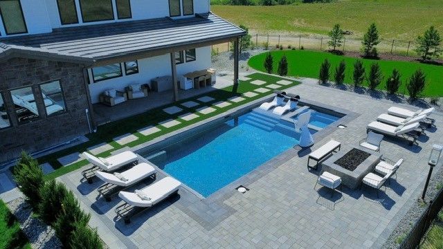 Aerial view of a backyard with a pool, patio furniture, and a modern house with a stone exterior.