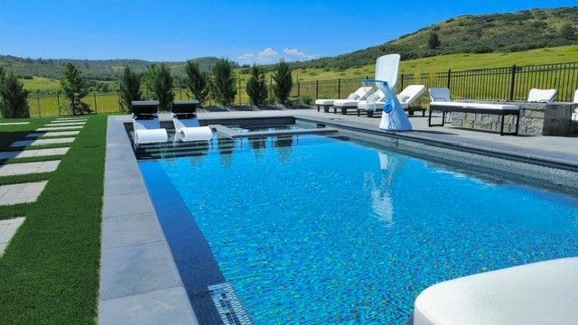 Poolside scene: blue pool, lounge chairs, green grass, and a sunny day.