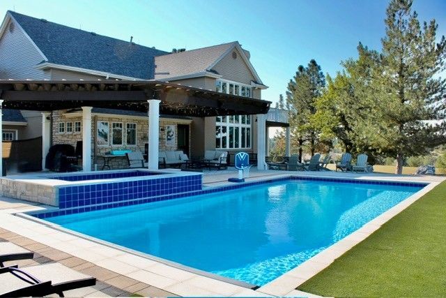 Backyard pool with a house, a hot tub, and a pergola under a bright blue sky.