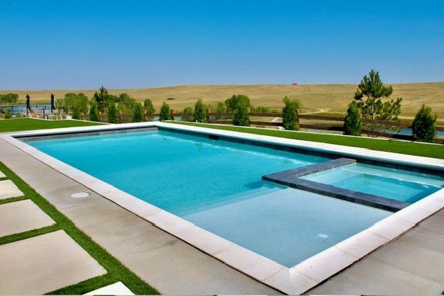 Rectangular swimming pool with attached hot tub; blue water, blue sky, and grassy landscape.