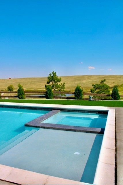 Swimming pool with a jacuzzi, set against a grassy hill and blue sky.