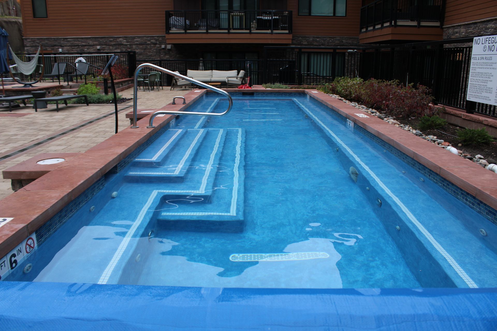 Outdoor rectangular pool with stairs and a diving board.