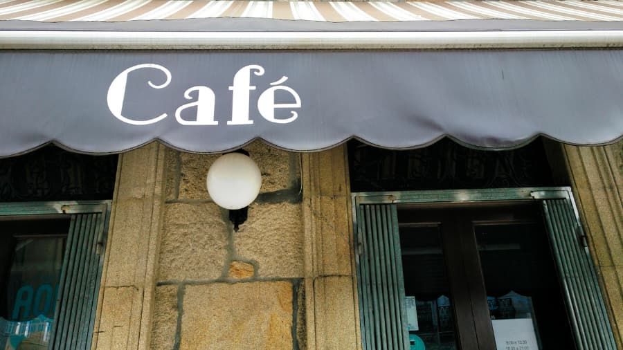 Cafe sign above a stone building entrance; a gray awning with scalloped edge.