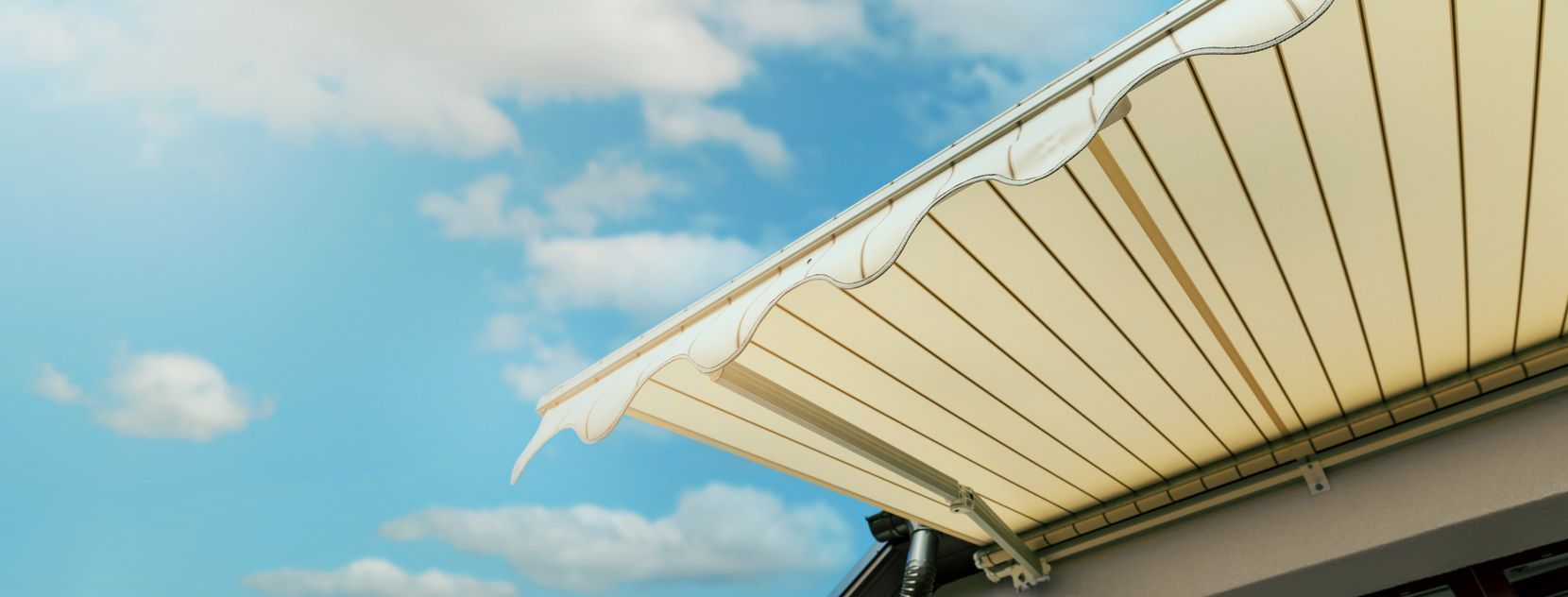 Beige awning against a blue sky with clouds.