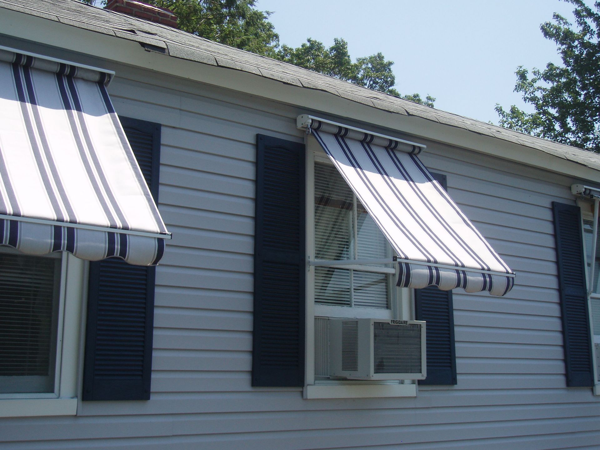 Red and white striped awnings above storefront windows on a brick building, with green gooseneck lights.