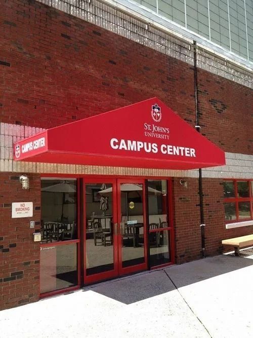 Campus Center entrance with red awning, St. John's University logo, red doors, and brick building.
