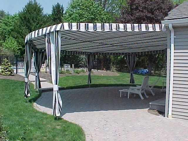 Patio with striped canopy and curtains, two white chairs on stone.