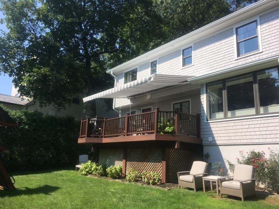 Backyard deck with a retractable awning, chairs, and a house with light gray siding.