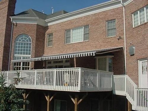 Brick house with a wooden deck and awning, viewed from the backyard.