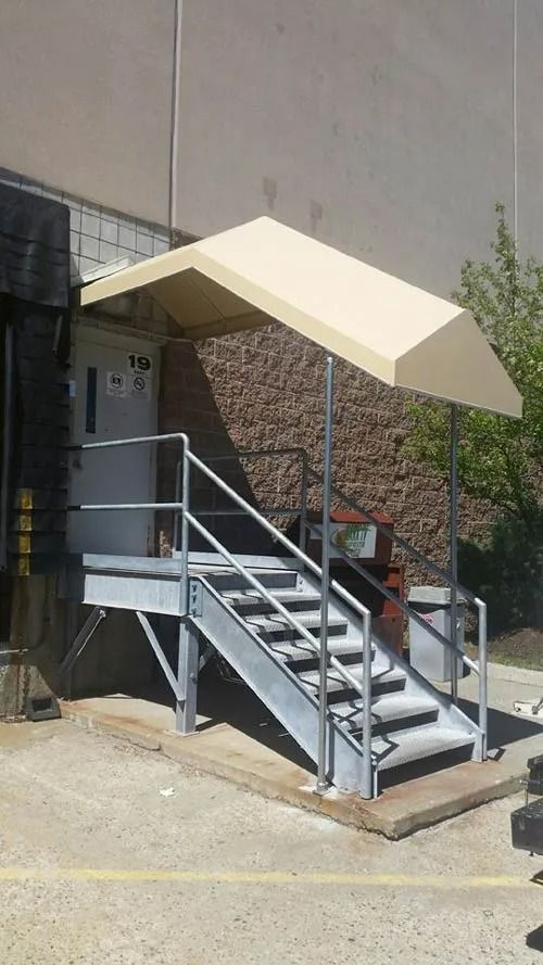 Metal stairs with handrails lead to a door under a beige awning.
