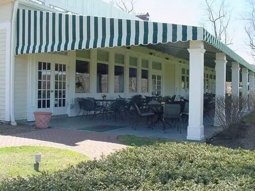 Outdoor patio with green and white striped awning and tables, chairs, and shrubbery.