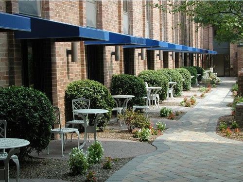 Brick building with blue awnings, small white tables and chairs, and a paved walkway.