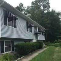 Light blue house with black awnings, surrounded by trees and greenery.