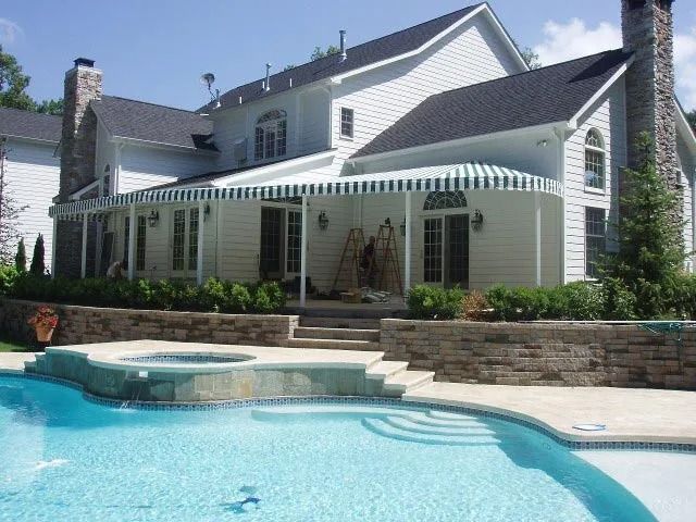 Back view of a large, white house with a pool, patio and green and white awning.