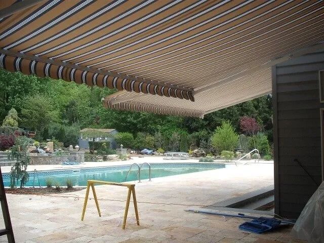 Beige and brown striped awning over a pool patio with a pool in the background.